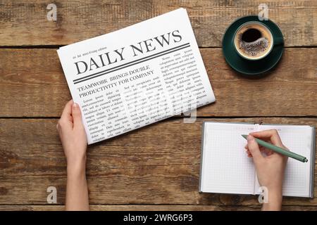 Mani femminili con il giornale che scrivono qualcosa su sfondo di legno. Vista dall'alto Foto Stock