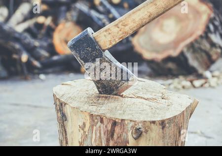 Vecchia, usurata, graffiata e affilata ascia su un ceppo d'albero di legno incrinato su uno sfondo di legno tritato. Foto Stock