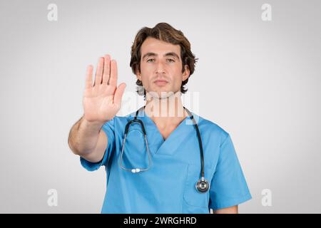 Maschio medico professionista in scrub blu gesturing stop Foto Stock