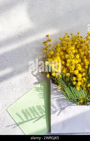 Vista dall'alto di un mazzo di fiori di mimosa gialli che fuoriescono da una busta con un biglietto bianco Foto Stock
