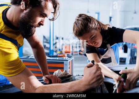 Riparatori esperti in un'officina di riparazione auto che lavorano insieme per la riparazione della vettura, discutendo le opzioni migliori. I dipendenti del lavoro di squadra che collaborano alla manutenzione del veicolo rotto, controllando la presenza di batteria guasta Foto Stock