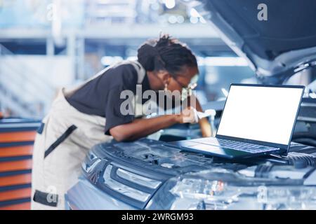 Mockup laptop accanto al meccanico che sostituisce il vecchio liquido della trasmissione dell'auto con uno nuovo in officina. Dispositivo di controllo isolato e dipendente del garage che utilizza attrezzature professionali per il controllo del veicolo Foto Stock
