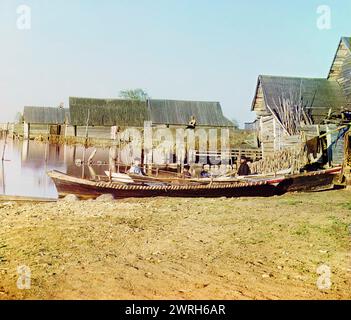 Embankment of Lake Seliger: "Insediamenti di pesca sul lago Seliger", 1910. Uomini in barche da pesca sulla riva di un villaggio di pescatori, con reti da pesca che si asciugano sullo sfondo. Foto Stock