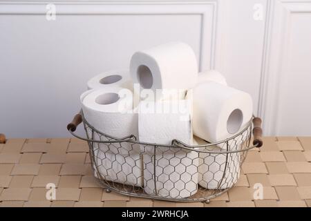 Rotoli di carta igienica morbida in cestello metallico su tavola di vimini, primo piano Foto Stock