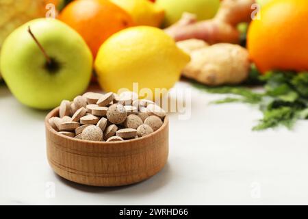 Integratori alimentari in ciotola di legno e prodotti su tavola bianca, primo piano. Spazio per il testo Foto Stock