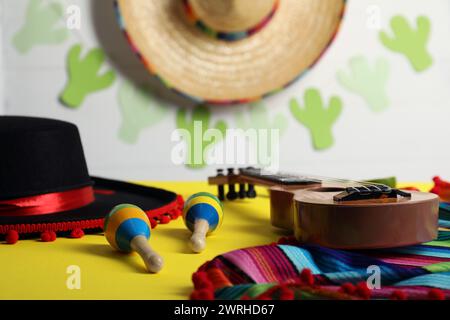 Cappello Flamenco nero, poncho, ukulele e maracas sul tavolo giallo, primo piano Foto Stock