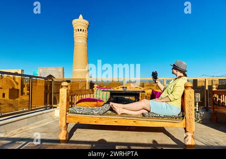 Donna turistica con classe piena di fichi al tavolo letto topchan al ristorante sul tetto a Bukhara vicino al minareto di Kalyan e alla madrasa in Uzbekistan Foto Stock