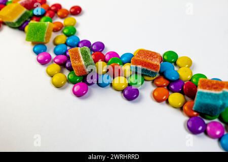 Una raffica di caramelle colorate in varie forme e dimensioni, sparse su uno sfondo bianco e pulito Foto Stock