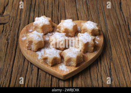 Un lotto di biscotti di pasta frolla di alfajores appena sfornati a forma di stelle su un piatto di legno a cuore. Foto Stock