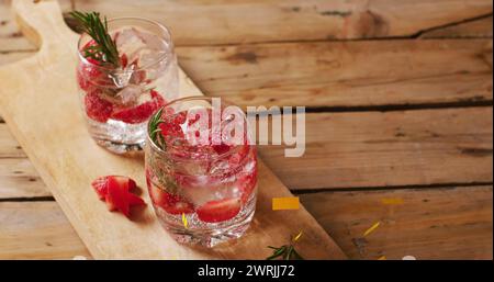 Due cocktail rinfrescanti guarniti con rosmarino e fragole su una tavola di legno Foto Stock