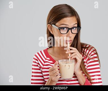 Donna, ritratto e caffè ghiacciato che beve in studio o bevanda dolce per il fine settimana rilassante, caffeina o sfondo grigio. Donna, bicchieri e latticini Foto Stock