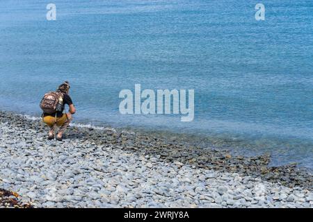 Kapiti Island - nuova Zelanda - febbraio 26 2024; donna con zaino accovacciato da mangiatori bordo per scattare foto con il telefono cellulare Foto Stock