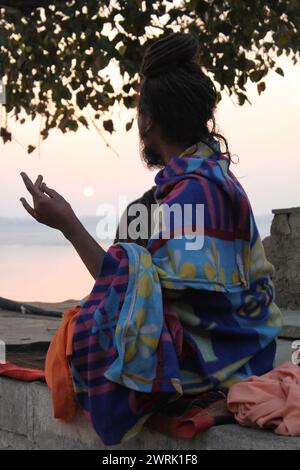 Varanasi, India - 13 marzo 2019: Uno yogi media all'alba con vista sul fiume santo Gange a Varanasi. Uomo, seduto, coperto di coperte Foto Stock