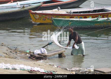 Varanasi, India - 13 marzo 2019: Una lavatrice (conosciuta in India come dhobi) lavora all'aperto per pulire vestiti e biancheria nel fiume Gange a Varanasi Foto Stock