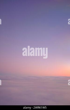 Cielo arancione al tramonto su un paesaggio nuvoloso visto dalla finestra di un aeroplano su un paesaggio innevato Foto Stock