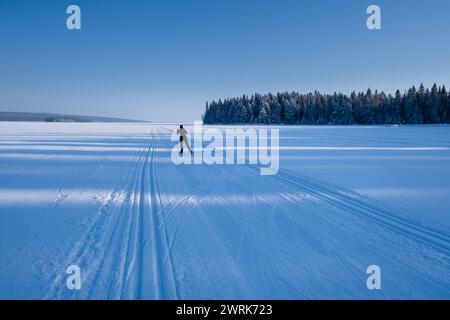 SCIATORE SOLITARIO, PISTE DA SCI PUBBLICHE, LAGO FROZEN, FINLANDIA: Uno sciatore solitario si dirige verso il sole invernale su piste da sci pubbliche comuni per lo sci di fondo sul lago invernale ghiacciato di Kaaani, nella Finlandia centrale. La città di Kajaani e la regione circostante di Kainuu sono un tranquillo paradiso di autentica vita finlandese nella tranquillità e nella bellezza naturale del cuore della Finlandia. Lo splendido paesaggio naturale, compreso il bellissimo lago Oulujärvi, offre uno sfondo idilliaco per attività all'aperto, tra cui pesca, escursioni, sci e motoslitta. Foto Stock