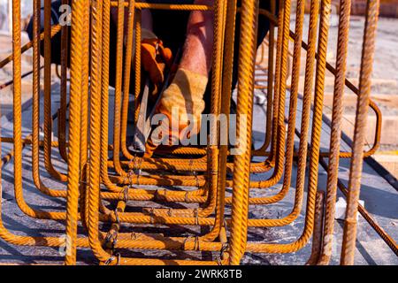 Il lavoratore sta legando il tondino con il filo utilizzando delle pinze, per realizzare un telaio di rinforzo per travi in calcestruzzo. Lavori in cantiere Foto Stock