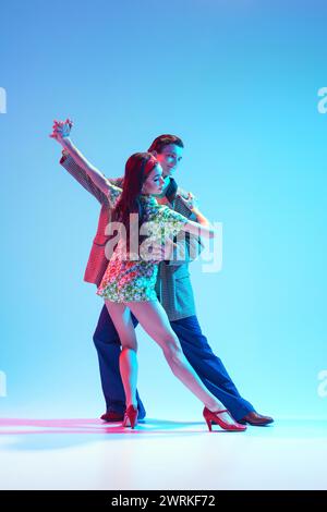 Bella, elegante ed elegante giovane coppia, uomo e donna che ballano rétro su sfondo blu con luce al neon Foto Stock