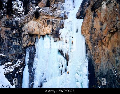 Vista aerea con droni dell'atleta che scalava il ghiaccio, la grande cascata ghiacciata nella gola di Barskoon, la valle di montagna nella parte meridionale del lago Issyk Kul, Kirghizistan Foto Stock