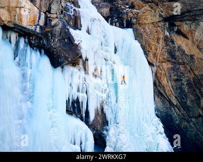 Veduta aerea dell'atleta in giacca arancione arrampicata su ghiaccio presso la grande cascata ghiacciata nella gola di Barskoon, la valle di montagna in Kirghizistan Foto Stock