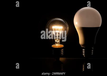 Due lampadine su sfondo nero, una lampadina a incandescenza è accesa e una lampada a LED. concetto di tecnologia elettrica. Foto Stock