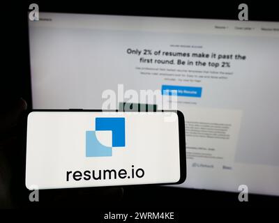 Persona che detiene un telefono cellulare con il logo della società olandese Resume.io di fronte alla pagina Web aziendale. Mettere a fuoco il display del telefono. Foto Stock