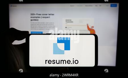 Persona che detiene un cellulare con il logo della società olandese Resume.io di fronte alla pagina Web aziendale. Mettere a fuoco il display del telefono. Foto Stock