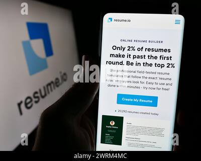 Persona che detiene un cellulare con la pagina web della società olandese Resume.io di fronte al logo aziendale. Messa a fuoco al centro del display del telefono. Foto Stock