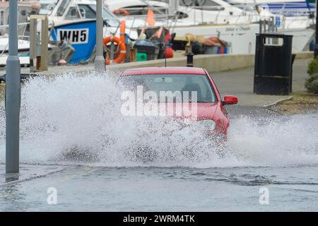 Weymouth, Dorset, Regno Unito. 13 marzo 2024. Meteo nel Regno Unito: Un'auto attraversa l'acqua alluvionale da un'alta marea primaverile su Commercial Road vicino al porto di Weymouth nel Dorset in una calda mattinata ricoperta. Crediti fotografici: Graham Hunt/Alamy Live News Foto Stock