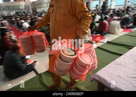 I devoti musulmani si siedono insieme prima di rompere il digiuno durante il mese Santo del Ramadan alla Moschea Nazionale Baitul Mukarram a Dacca, Bangladesh, il 13 marzo 2024 Foto Stock