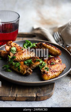 Ali di pollo arrosto in salsa piccante, guarnite con coriandolo fresco, presentate su un piatto con un bicchiere di cocktail di ciliegia su un rustico tavolo di legno. Foto Stock