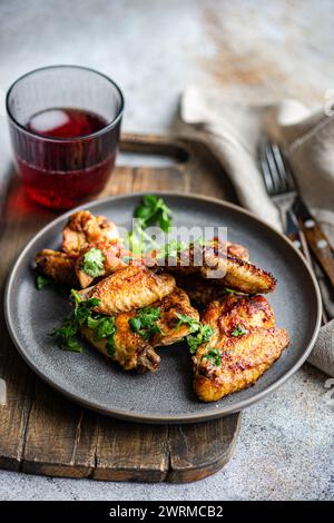 Deliziose ali di pollo arrosto in salsa piccante guarnite con coriandolo fresco. Servito su un piatto grigio con un cocktail di ciliegia a lato. Foto Stock