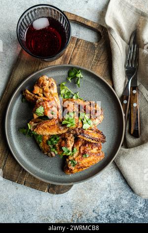 Vista dall'alto succulente ali di pollo arrosto in salsa piccante guarnite con foglie di coriandolo fresche, servite insieme a un rinfrescante bicchiere di cocktai di ciliegia Foto Stock