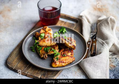 Ali di pollo arrosto croccanti condite con salsa piccante e guarnite con coriandolo fresco, accompagnate da un cocktail di ciliegia in un bicchiere, presentato su una Foto Stock