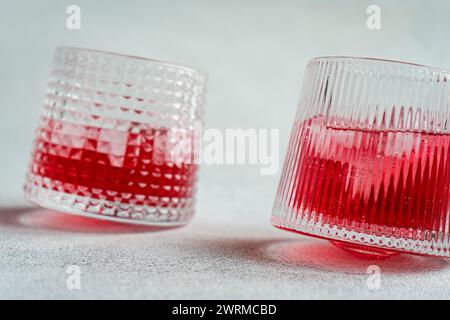 Due bicchieri testurizzati riempiti di ghiaccio e una vivace vodka alla ciliegia e un cocktail tonico, realizzati su uno sfondo semplice. Foto Stock