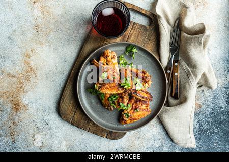 Vista dall'alto ali di pollo arrosto in salsa piccante guarnita con coriandolo fresco, presentato su un piatto accanto a un bicchiere di cocktail di ciliegia, con cutler Foto Stock