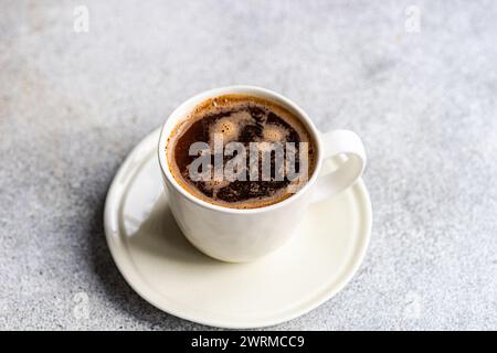 A dall'alto di una tazza di caffè nero appena estratto, con bolle visibili, servito in una tazza di ceramica bianca seduta su un piattino coordinato, su un textur Foto Stock