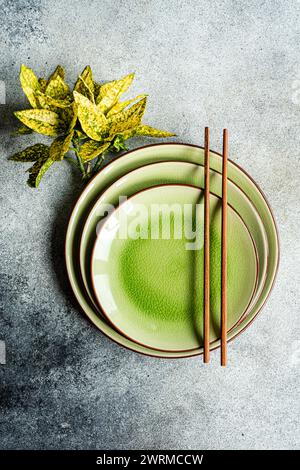 Dall'alto, un tavolo ben organizzato con piatti di ceramica verde vibrante e bacchette marroni, accompagnati da una pianta decorativa su un textur Foto Stock
