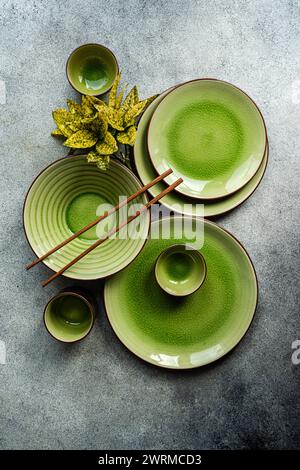 Vista dall'alto di un elegante tavolo con stoviglie in ceramica verde brillante e posate in legno su una superficie grigia testurizzata. Foto Stock
