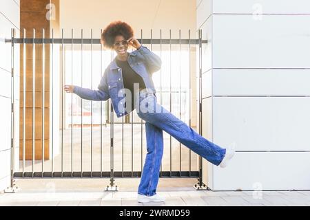 Una donna catturata a metà volteggio gode di un momento di divertimento con il suo abito in denim, mentre la luce del sole aggiunge una luce gioiosa alla scena Foto Stock