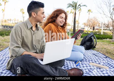Diversi studenti si sono impegnati a studiare con un notebook e un tablet durante un picnic al parco, mostrando tecnologia e istruzione all'aperto. Foto Stock