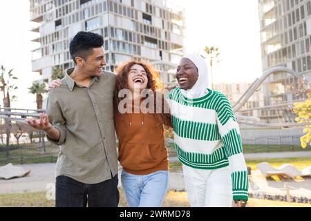 Un gruppo di tre studenti gioiosi, tra cui un uomo latino, una donna afroamericana, una donna caucasica, che condividono un momento felice in un parco urbano Foto Stock