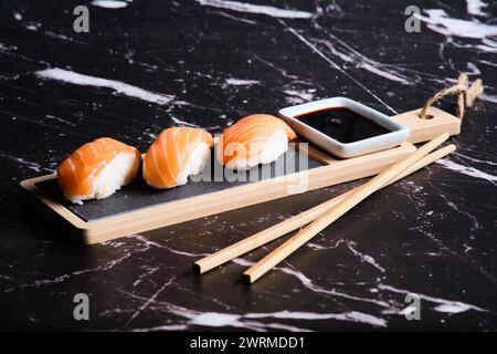 Tre pezzi di sushi di salmone serviti su un tavolo di legno con salsa di soia e bacchette su sfondo marmorizzato. Foto Stock