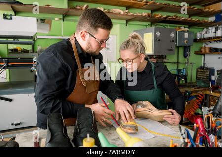 Due calzolai, un uomo e una donna, stanno lavorando insieme su una scarpa in un'officina ben attrezzata in Austria, circondata da attrezzi e macchinari. Foto Stock