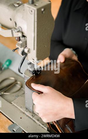 Primo piano delle mani anonime del calzolaio che realizzano una scarpa in pelle utilizzando una macchina da cucire in un'officina austriaca. Foto Stock