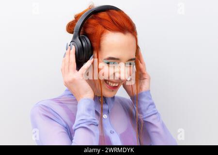 Una giovane donna d'affari caucasica che sorride mentre ascolta musica con le cuffie. I suoi occhi sono delicatamente chiusi, accentuati dall'ombra turchese Foto Stock