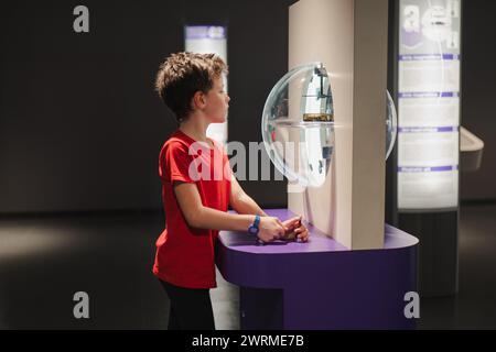 Un ragazzo curioso con una camicia rossa è impegnato in una mostra scientifica interattiva, che mostra fascino e gioia di imparare. Foto Stock