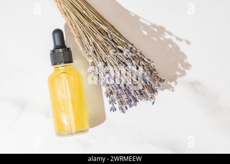 Accanto a un bouquet di lavanda secca si trova una bottiglia trasparente piena di essenza d'olio color oro, che suggerisce bellezza e relax biologici Foto Stock