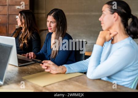 Tre donne professionali impegnate in una riunione d'affari, con una che guarda la telecamera. Foto Stock