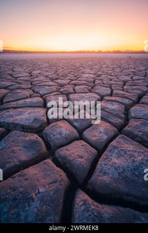 Le sfumature radiose di un sole che tramonta illuminano gli intricati schemi di profonde crepe di fango, creando un contrasto tra terra arida e un cielo vibrante Foto Stock